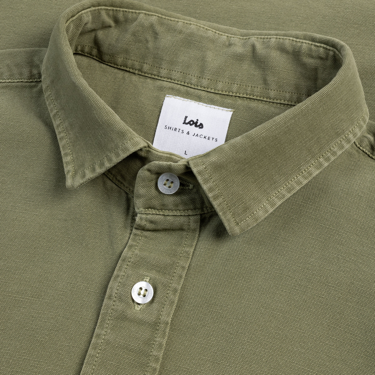 Close-up of a green shirt collar with buttons and a visible label on a green background.