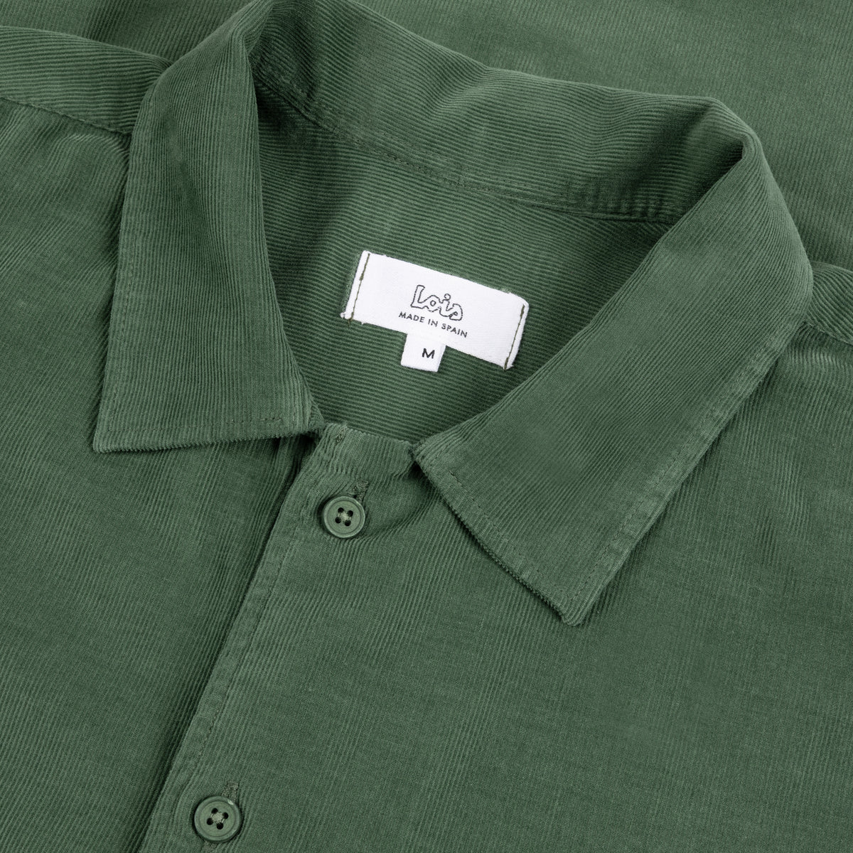 Close-up of a dried herb corduroy long sleeve shirt collar with a white brand label reading 'Lois' and size 'M'.