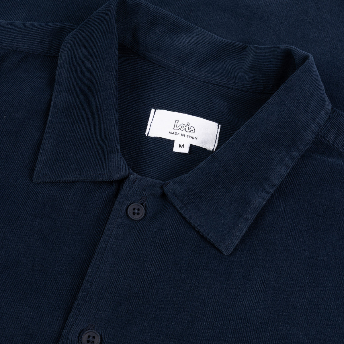 Close-up of a dark navy corduroy shirt collar with a white neck label reading 'Lois MADE IN SPAIN' and size 'M'.