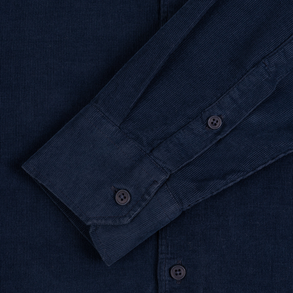 Close-up of a dark navy corduroy shirt showing the fabric texture, buttoned cuff, and front placket.
