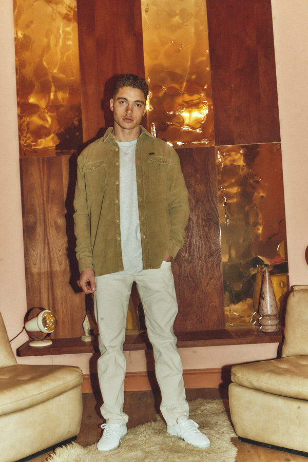 A long-sleeve corduroy button-up shirt in a warm khaki-beige color, featuring two buttoned chest pockets and a small black brand tab on the left chest, displayed flat against a white background.